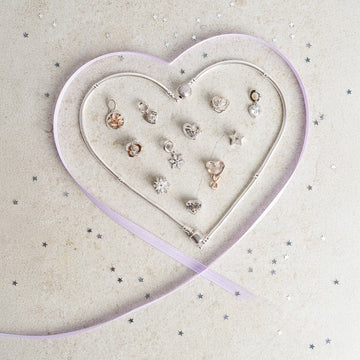 Charms aus 925 Silber und Roségold mit Charm-Armbändern als Herzform gelegt mit lila Schleife und Sternenkonfetti