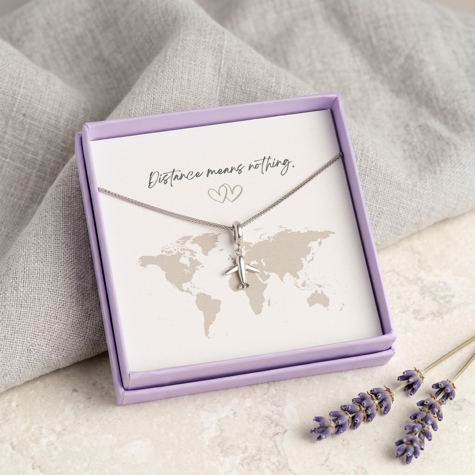 Kette mit Flugzeug-Anhänger aus 925 Silber in Geschenkbox vor Weltkarten-Motiv, Geschenkkarte "Distance means nothing"