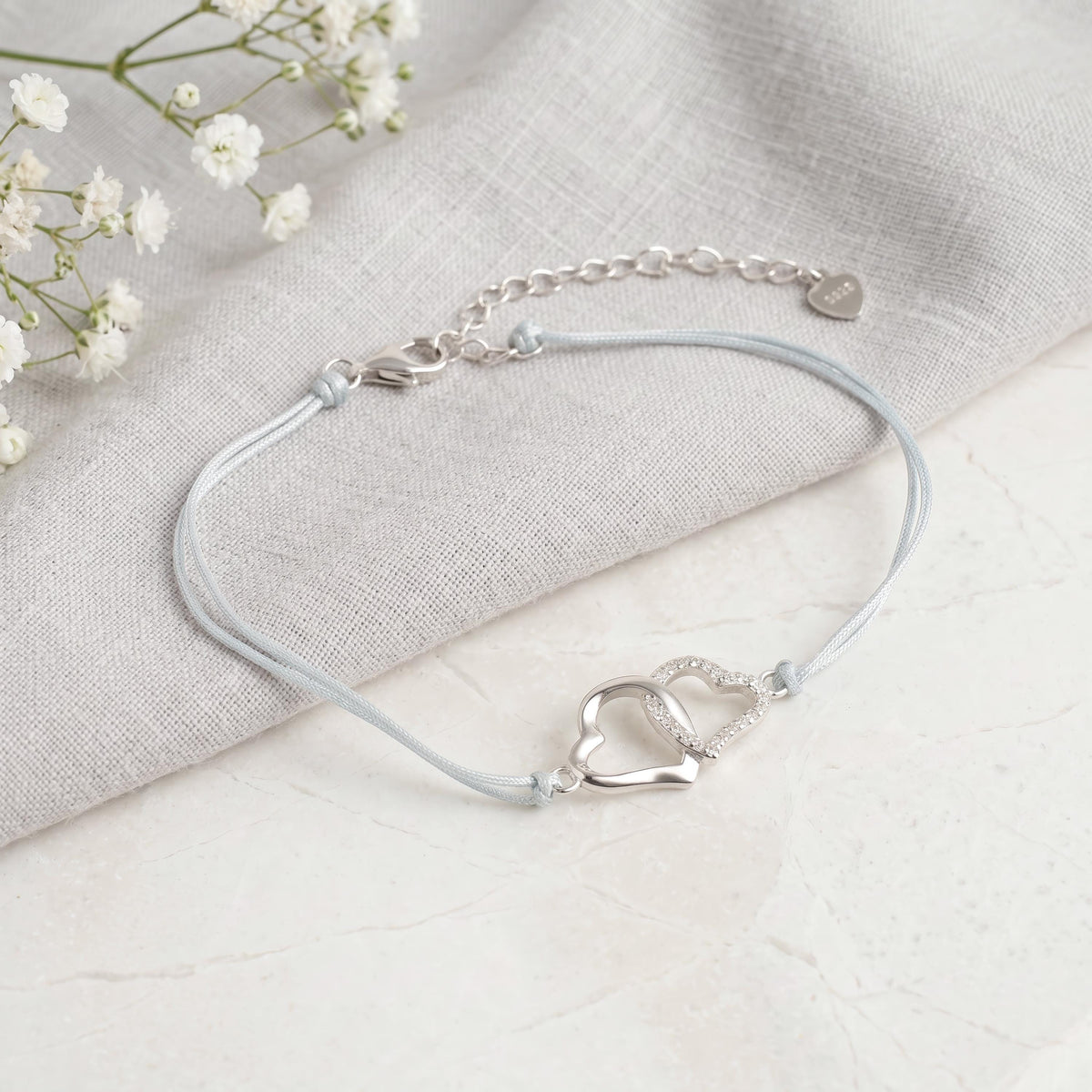 Segeltau-Armband mit zwei verschlungenen Herzen aus 925 Silber, auf Leinenstoff mit Schleierkraut drapiert