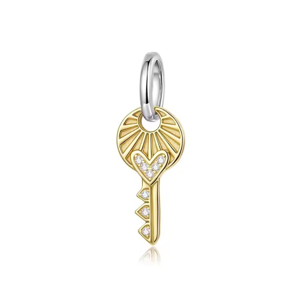 Goldfarbener Schlüssel-Charm aus 925 Silber und 18 K Gold mit Herzmotiv, funkelnden Zirkonia-Steinen und silberfarbener Öse.